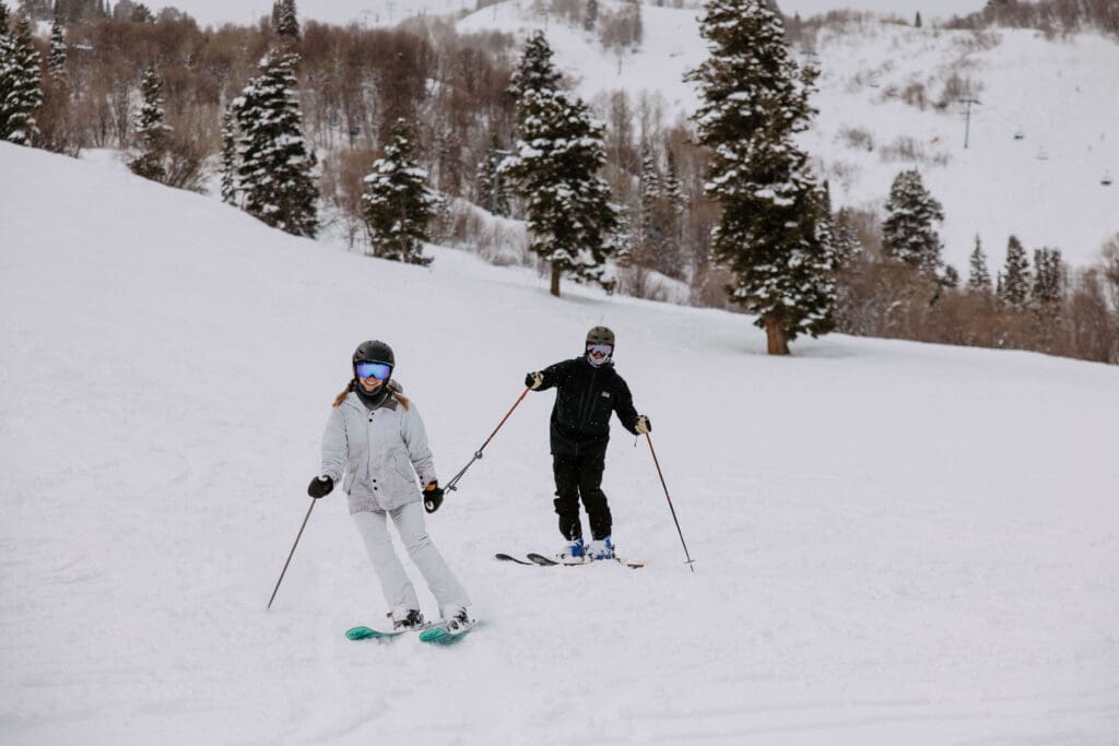 Bride and groom hit the slopes at Snowbasin Ski Resort during their winter elopement, surrounded by snowy pine trees and mountain peaks.