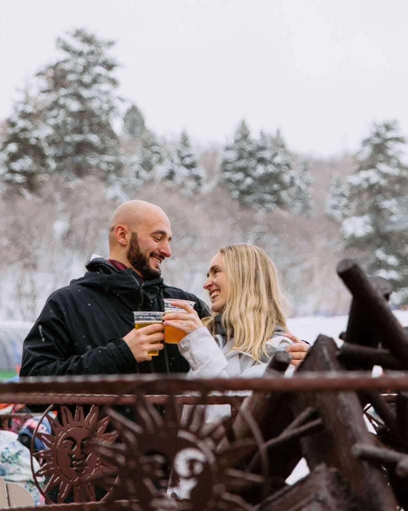 Couple enjoys local craft beers around the fire on their snowy elopement day at Snowbasin Ski Resort