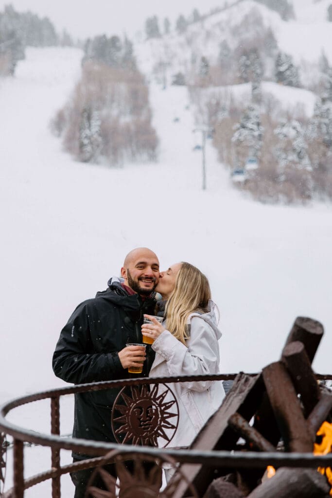Couple enjoys apres-ski around the fire with local craft beers on their wedding day at Snowbasin Ski Resort, captured by Utah elopement photographer Bri Parkin.