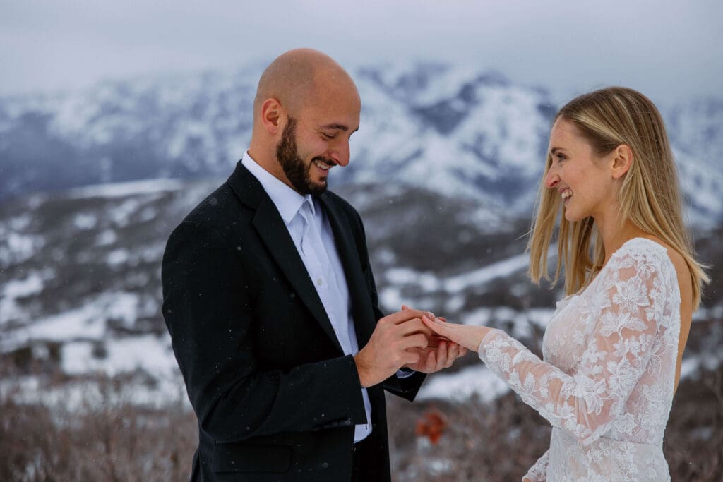 bride and groom exchange rings with views of Snowbasin Ski Resort behind them