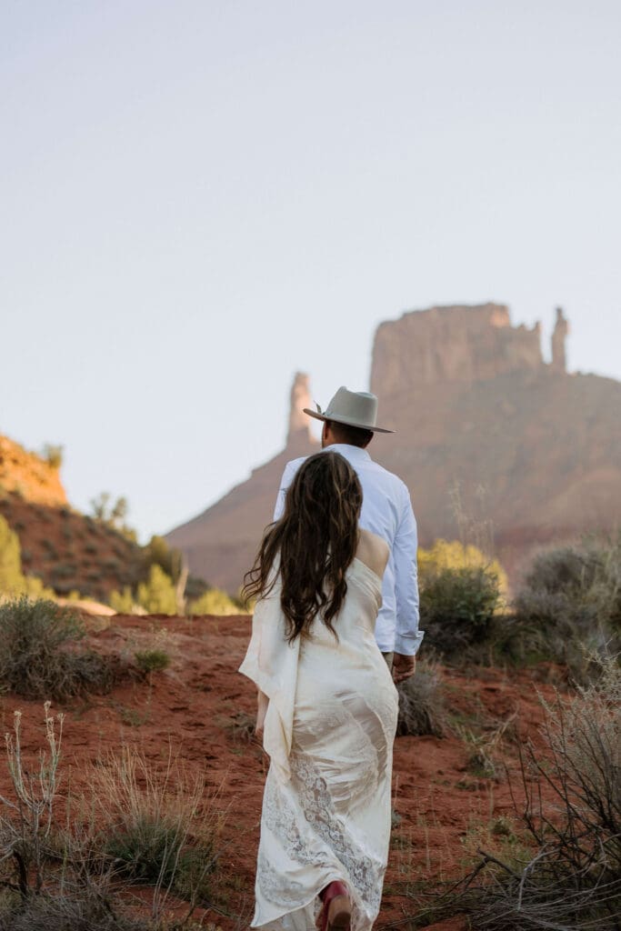 bride and groom walk through red rock desert in moab