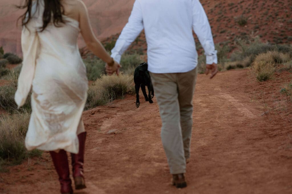 bride and groom walk through the moab desert with their dog