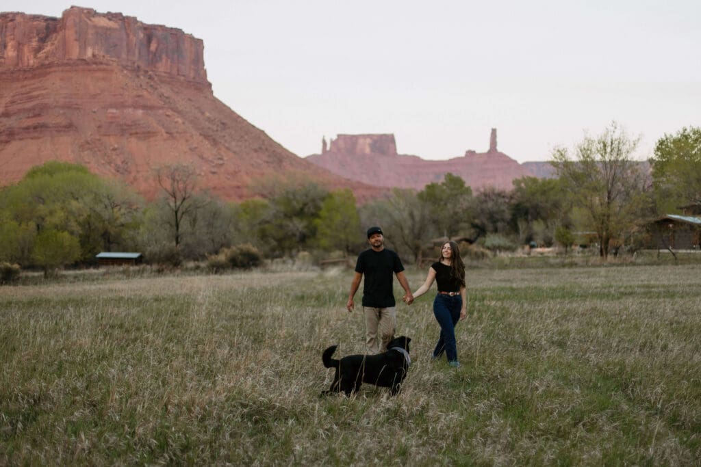 couples walks through field in cast valley with their dog