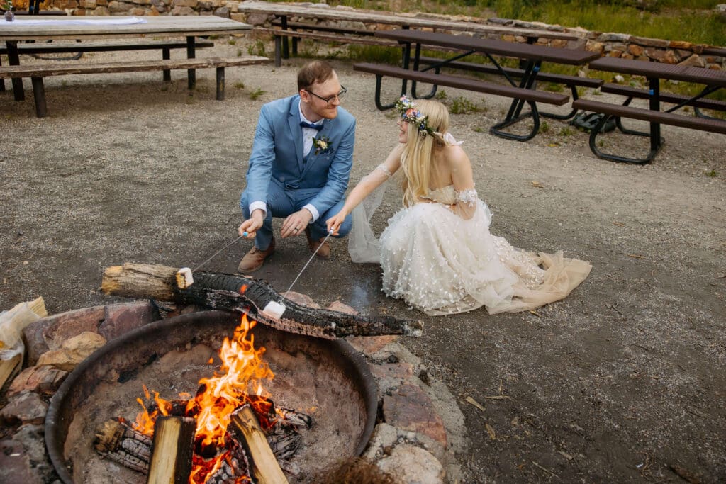 bride and groom roasting marshmallows over campfire
